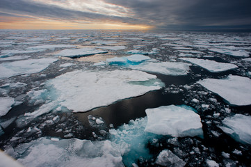 Northern Arctic ice floes are seen breaking up and melting leading into an atmospheric moody horizon with sunset.Climate crisis emergency and global warming.Image © Tony Skerl