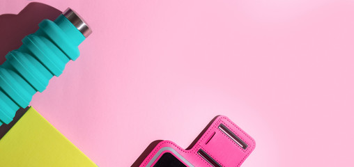 flat lay sport fitness run blue water bottle, diary green and hot pink phone holder on a pink background