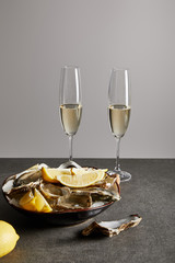 champagne glasses with sparkling wine near delicious oysters and lemons in bowl isolated on grey