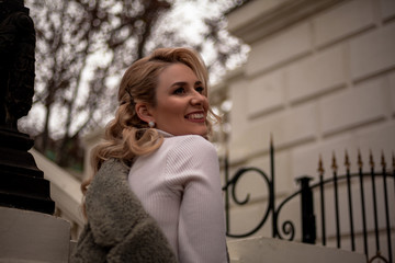 Fototapeta premium Fashion european woman walking at the street, dressed modern clothes. Female moder wearing faux fur coat, tutleneck, skirt, and curl hairstyle