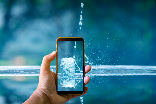 Hand holding mobile phone and take a photo Drink water pouring in to glass over sunlight and natural green background.Water splash in glass Select focus blurred background.
