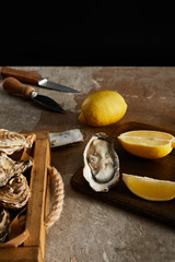 selective focus of delicious oysters near lemons and knifes isolated on black