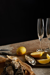 selective focus of oysters in shells near lemons on wooden cutting board and champagne glasses...