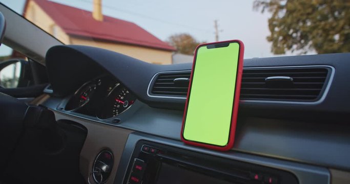 Close up of blank green screen smart phone on dashboard panel in moving driving car. Navigating app. Chroma key mock-up. Business journey. Social network online. Gps map application. Internet search.