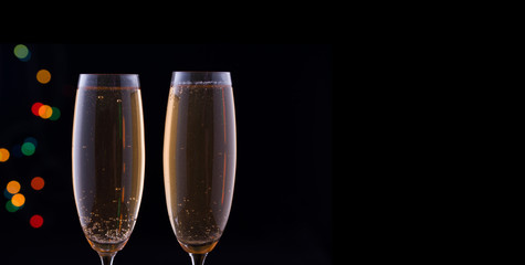Two glasses with champagne with festive lights on a dark background.