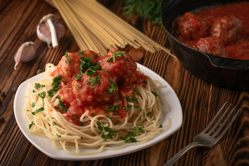 Plate of delicious spaghetti with meatballs and a frying pan for cooking