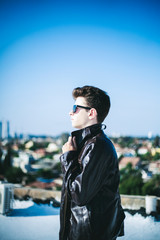 Young attractive man posing in front of camera in a dark  brown jacket on the roof of a residential building