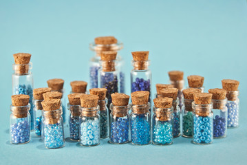 Purple and cyan beads in glass jars on bright blue background. Beads in a transparent container with a wooden cork. The concept of orderliness, balance and chaos.