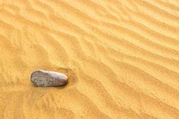 Fototapeta na wymiar Pebble lying on texture of yellow sand dunes. Can be used as natural background
