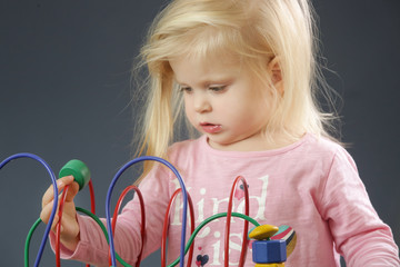 Toddler girl playing with wire bead maze toy. This colorful educational wooden toy teaches children hand-eye coordination, motor skills and colors.