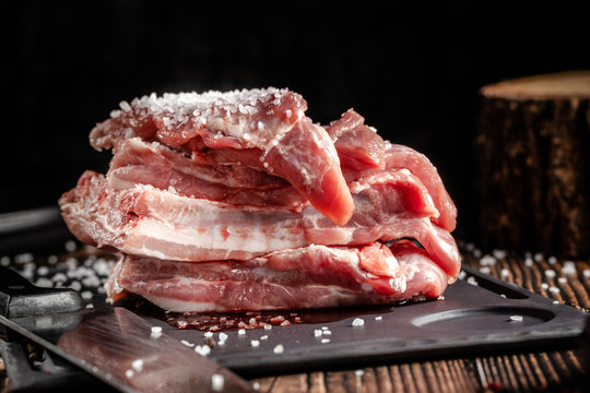 Raw pork meat lies on a cutting board, on a wooden table, next to a kitchen knife. Pickled meat in spices. Background image.