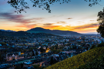 Germany, Magical city freiburg im breisgau skyline in warm sunset light in autumn season, aerial view above illuminated buildings of cityscape