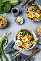 Asian style ramen noodle soup with bok choy, carrot, lime, sesame seeds, chicken and egg, gray background