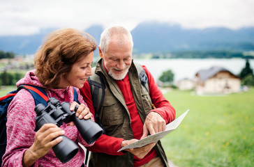 Senior pensioner couple with hiking in nature, using binoculars and map.