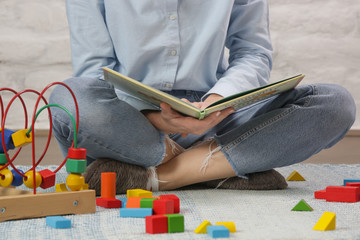 Mother or nanny sitting on the floor reading a book in a nursery room