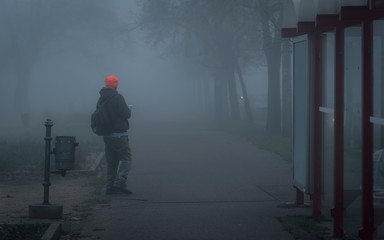Young man waiting for a bus or calling a taxi in the foggy city