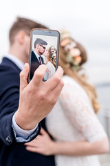 Küssendes Brautpaar fotografiert sich mit Smartphone