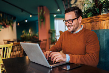 Cheerful freelancer working on laptop in the cafe, portrait.