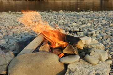 Bonfire burns on pebbles of a river bank, background