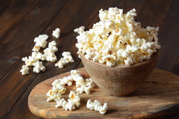Bowl with popcorn on wooden table. Bowl filled with popcorn spilled on table.