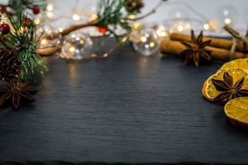 Obraz na płótnie Canvas Winter holiday still life concept on dark slate board with dried oranges, anise stars, cinnamon sticks and evergreen sprigs, room for text copy