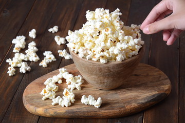 Bowl with popcorn on wooden table. Bowl filled with popcorn spilled on table.