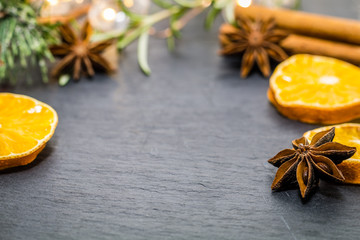 Winter holiday still life concept on dark slate board with dried oranges, anise stars, cinnamon sticks and evergreen sprigs, room for text copy