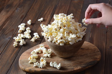 Bowl with popcorn on wooden table. Bowl filled with popcorn spilled on table.
