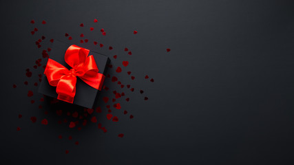 Merry Christmas and Happy Holidays. New Year. Valentine's day. Birthday. Black gift with red ribbon, present on black background top view.	
