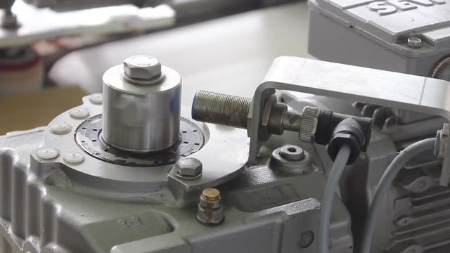A small shaft of great machinism rotates and the sensor fires. The sensor on the conveyor belt does its job. Close-up frame.