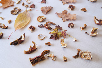 Dried mushrooms and autumn leaves on a background of white wood.	
