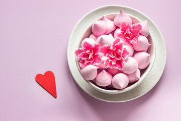 Small meringues and pink flowers in a ceramic bowl on pink paper background. Gift for Valentine's Day.