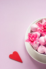 Small meringues and pink flowers in a ceramic bowl on pink paper background. Gift for Valentine's Day.