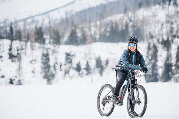 Female mountain biker with bicycle standing outdoors in winter nature.