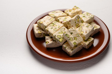 Eastern Arabic nougat sweetness with pistachios on a brown ceramic plate on a light background