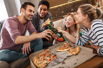 Group of friends making fun at the home party.They sitting in living room and eating pizza.	