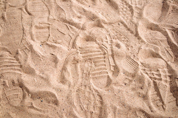 Sunlit sandy sea shore trampled by human footprints, may be used as background or texture