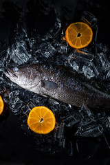 Fresh sea bass fish on ice on a black stone table top view