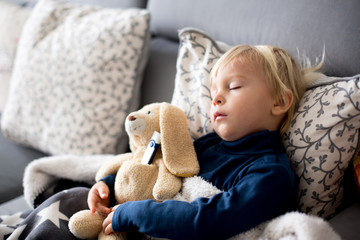 Blond toddler boy, sleeping on the couch in living room, lying down with fever