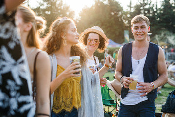 Group of young friends with drinks at summer festival, standing.
