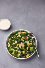 Kale cabbage salad with baked potatoes, cucumber, red onions and mustard yogurt sauce on gray texture background, top view, free space