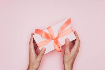 cropped view of man holding christmas gift box in hands, isolated on pink