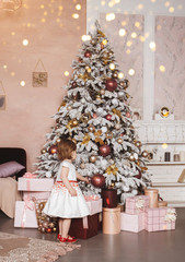 Christmas interior with decorated Christmas tree. A little girl in a white dress from the back. Holiday lights.