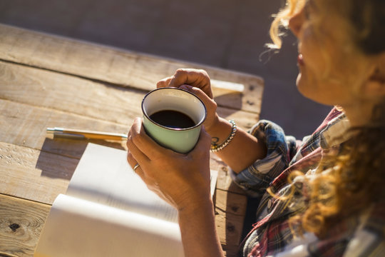 Close up of happy caucasian hands woman holding a cup of coffee and relaxing with white paper and penon a wooden table - concept of writer and old style lifestyle