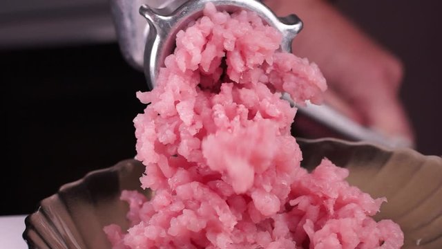 Cooking minced meat with a manual meat grinder. Close-up of front part of mincing-machine with mincemeat in. Showing the forcemeat process.