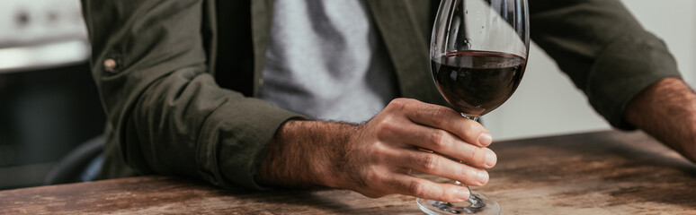 Cropped view of man holding wine glass at table, panoramic shot
