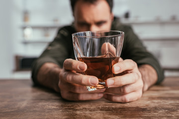 Selective focus of man holding whiskey glass in hands at table