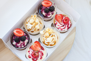 Mousse desserts in cup with cream cheese frosting, berry sauce, salted caramel, strawberry, cherry, raspberry and popcorn. 
