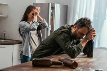 Selective focus of crying woman with alcohol addicted husband on kitchen