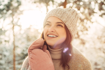 Happy young woman in a knitted hat and mittens in the sun in winter